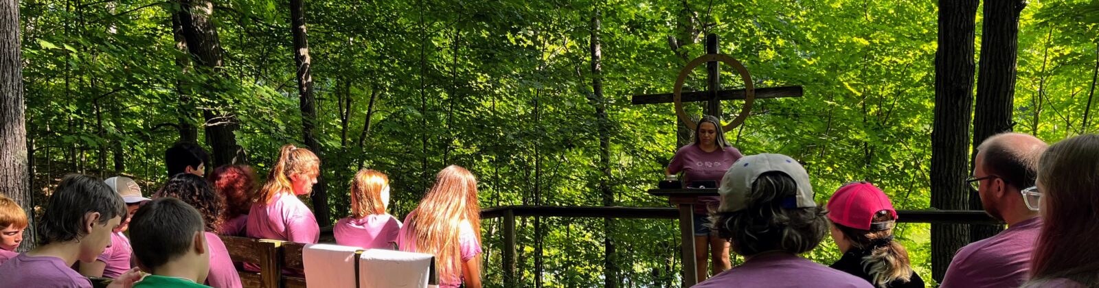 Photo of outdoor chapel at Camp Walter Scott. Students on wooden benches, with a backdrop of natural forest.